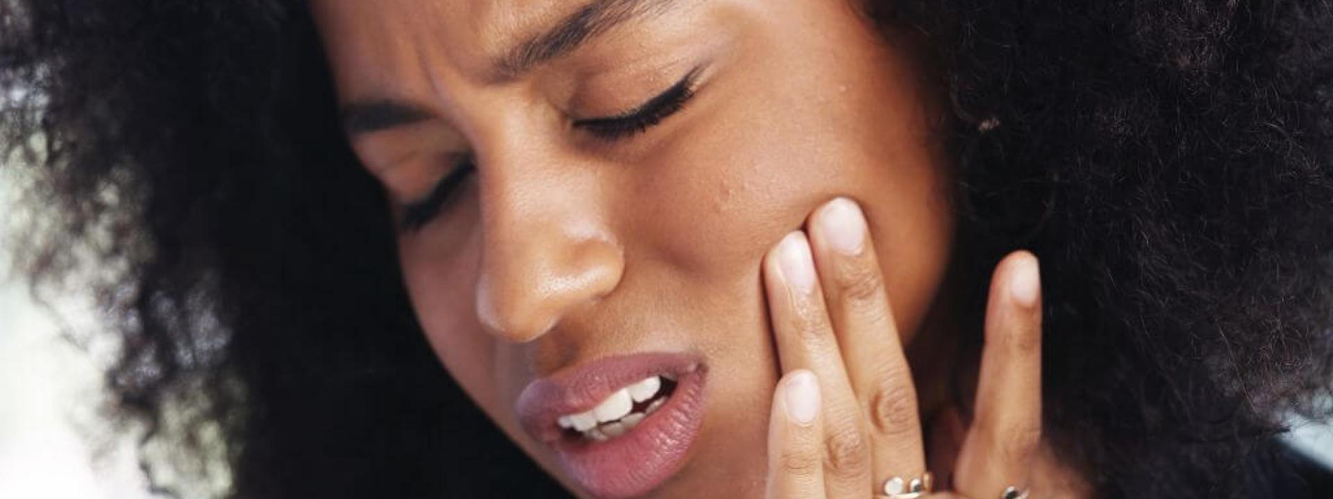 Woman having TMJ pain holding cheek.